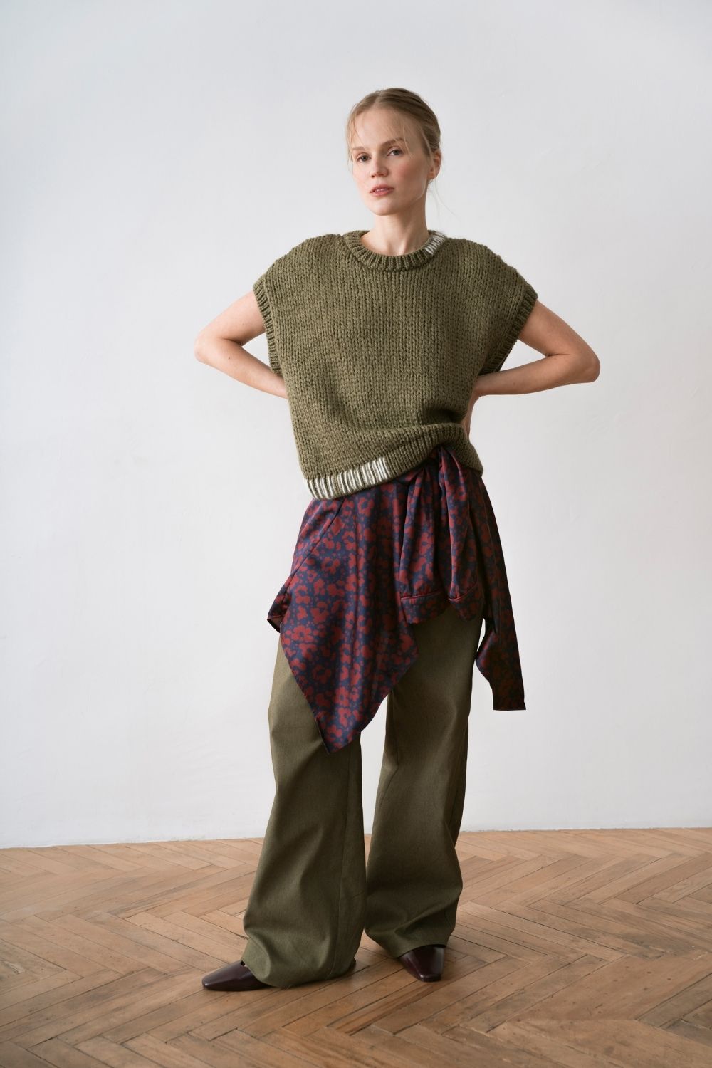 Paade Mode women collection look featuring an olive knitted sleeveless sweater, wide-leg green trousers and a burgundy patterned shirt tied at the waist, featured on Scimparello Magazine.