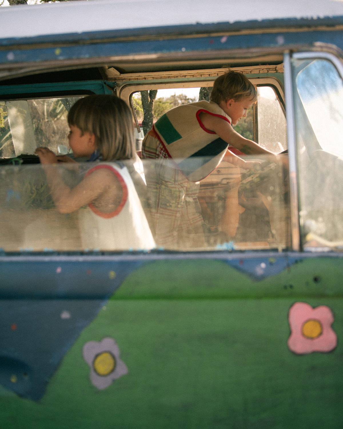 Two children playing inside a colorful vintage van while wearing handmade Playdate Vintage clothing crafted from reclaimed textiles for Scimparello Magazine.