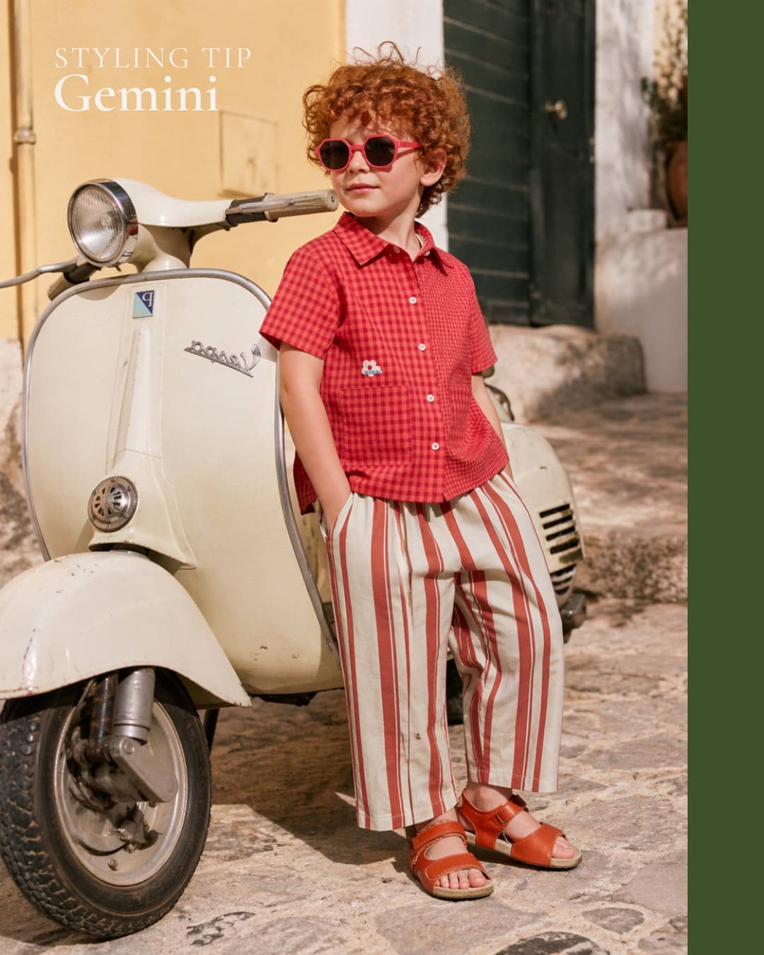 Curly-haired child wearing red gingham shirt, striped beige and red trousers, and red sandals, leaning against a vintage cream scooter, with pink sunglasses, in a sunny Mediterranean street setting.