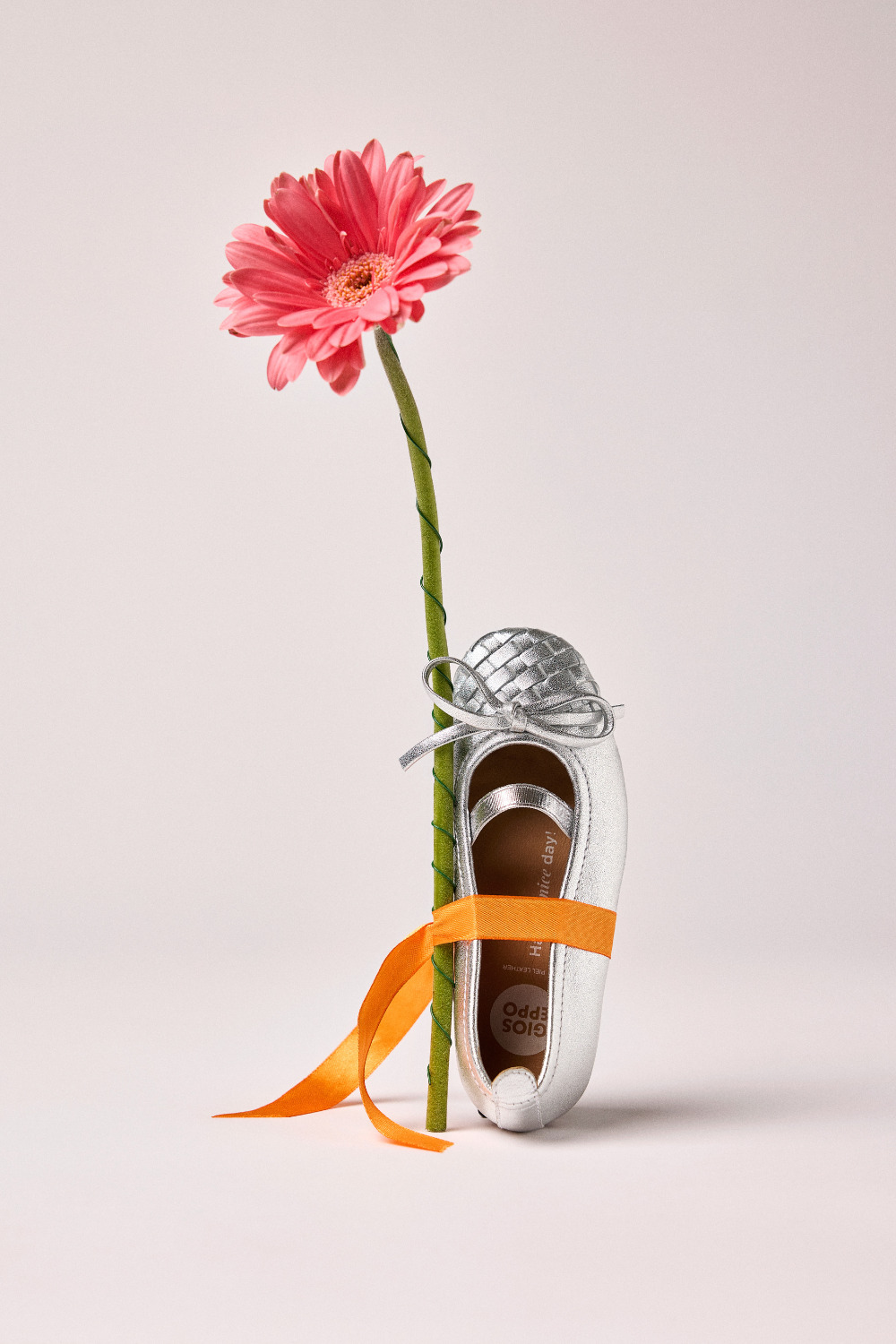 Silver Gioseppo Kids SS26 ballet flat tied with an orange ribbon beside a pink flower, featured on Scimparello Magazine.