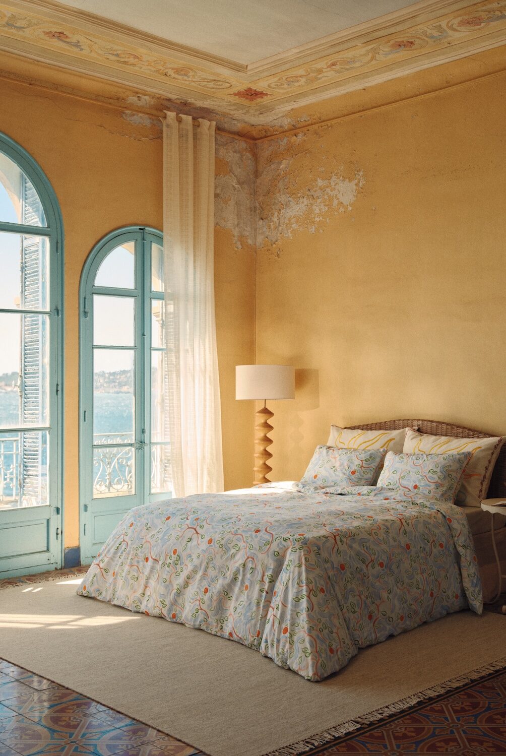 Sunlit Mediterranean-style bedroom featuring Bonsoirs x Jacques Merle illustrated bedding, soft pastel tones, vintage architectural details and French Riviera-inspired interiors.