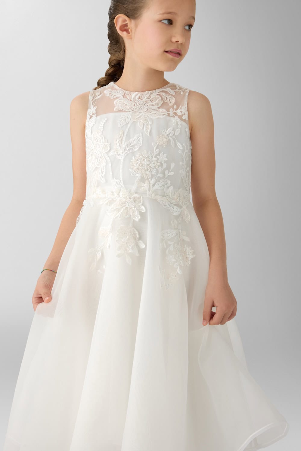 Close-up of a sleeveless white ceremonial dress featuring delicate floral embroidery, sheer neckline and voluminous skirt.