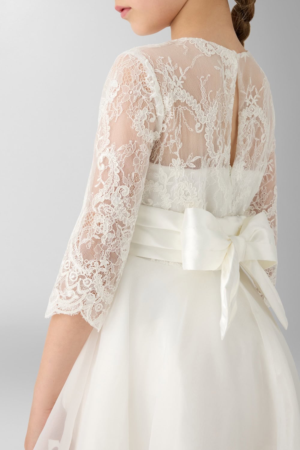 Back detail of an ivory dress with sheer lace sleeves, floral embroidery and oversized satin bow at the waist.