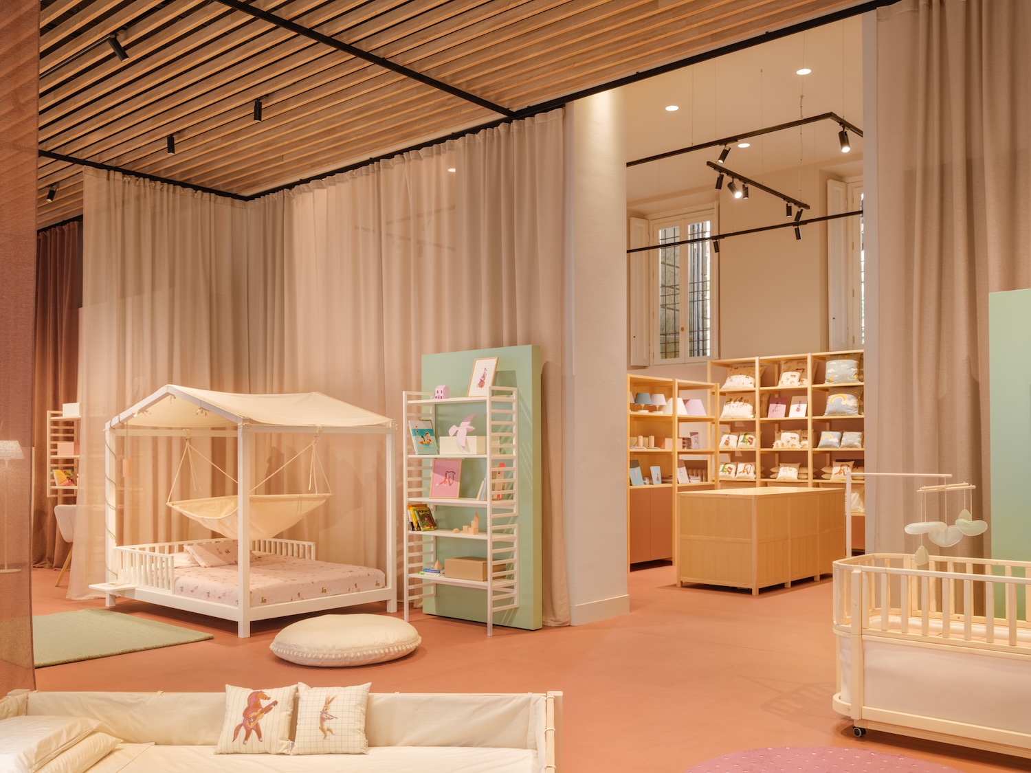 Interior view of Nabè’s flagship store in Milan featuring Montessori-inspired children’s furniture, pastel-colored décor, soft curtains, wooden details and a cozy canopy bed designed for modern family spaces.