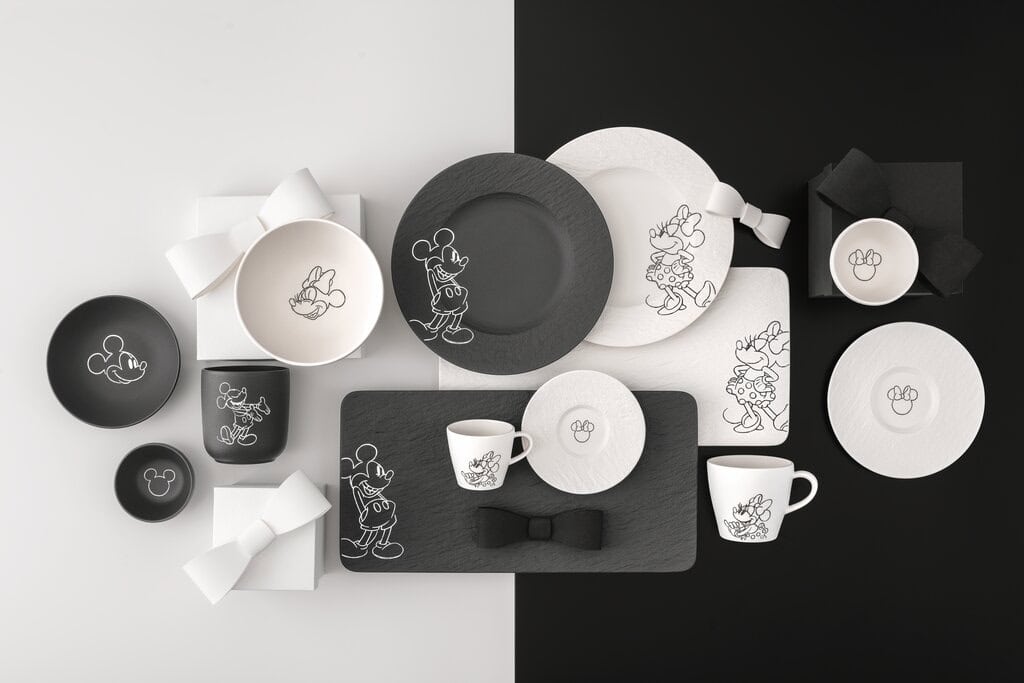 Flat lay of the Villeroy & Boch x Disney Manufacture – Mickey Mouse collection featuring black and white porcelain plates, bowls, and cups with sketch-style illustrations of Mickey Mouse and Minnie Mouse on a monochrome background.
