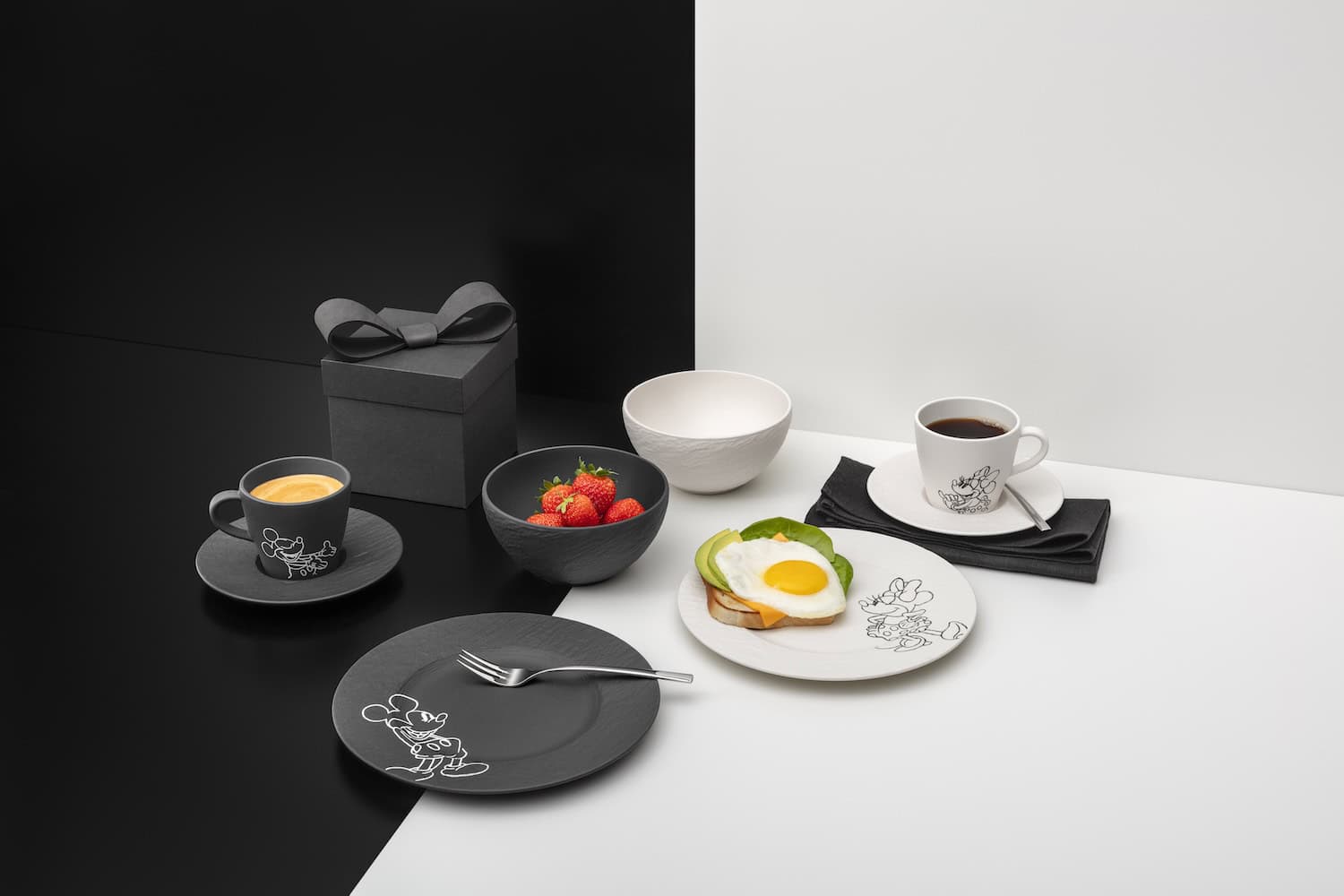 Contemporary breakfast scene featuring the Manufacture – Mickey Mouse porcelain collection by Villeroy & Boch, with black and white plates, coffee cups, strawberries, and Disney character illustrations styled in an elegant monochrome interior setting.