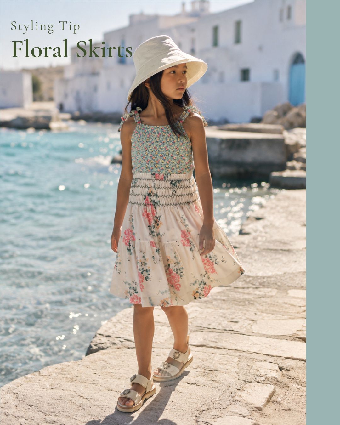 Girl wearing a floral skirt with a matching bathing suit, white sun hat and white sandals by the sea for a Styling Tip on floral skirts, Scimparello Magazine.