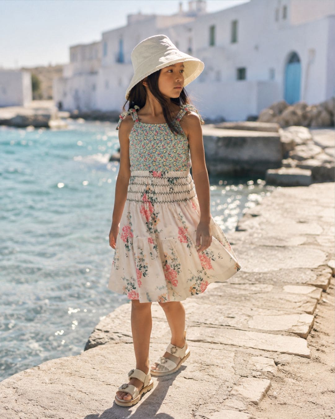 Girl wearing a floral skirt with a matching bathing suit, white sun hat and white sandals by the sea for a Styling Tip on floral skirts, Scimparello Magazine.
