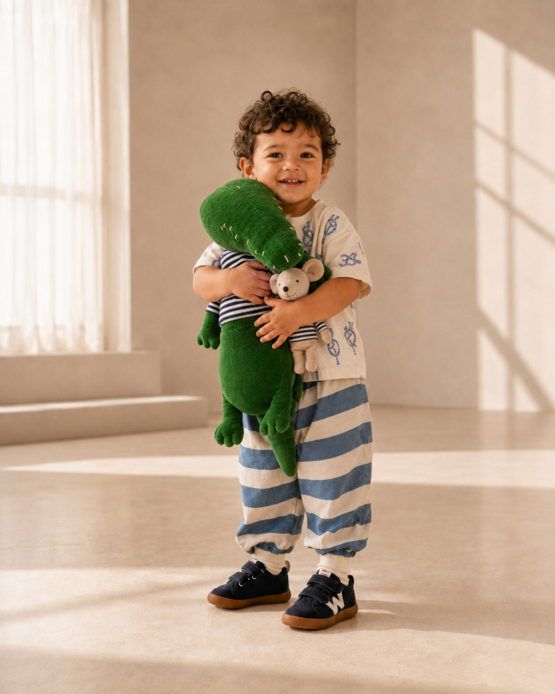 Smiling toddler wearing navy Walkey barefoot shoes with striped trousers, a printed summer shirt, and a plush crocodile toy in warm natural light, Scimparello Magazine.