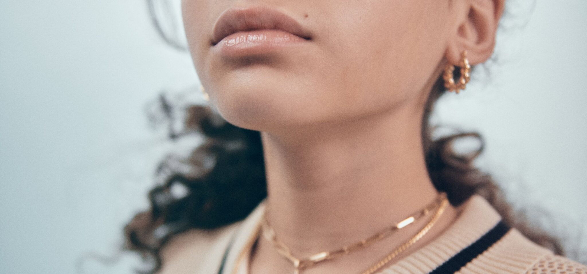 Close-up fashion detail of a child’s lips, gold earrings and layered gold necklaces in Faces, a kids fashion editorial photographed by Franck Malthierry for Scimparello Magazine.