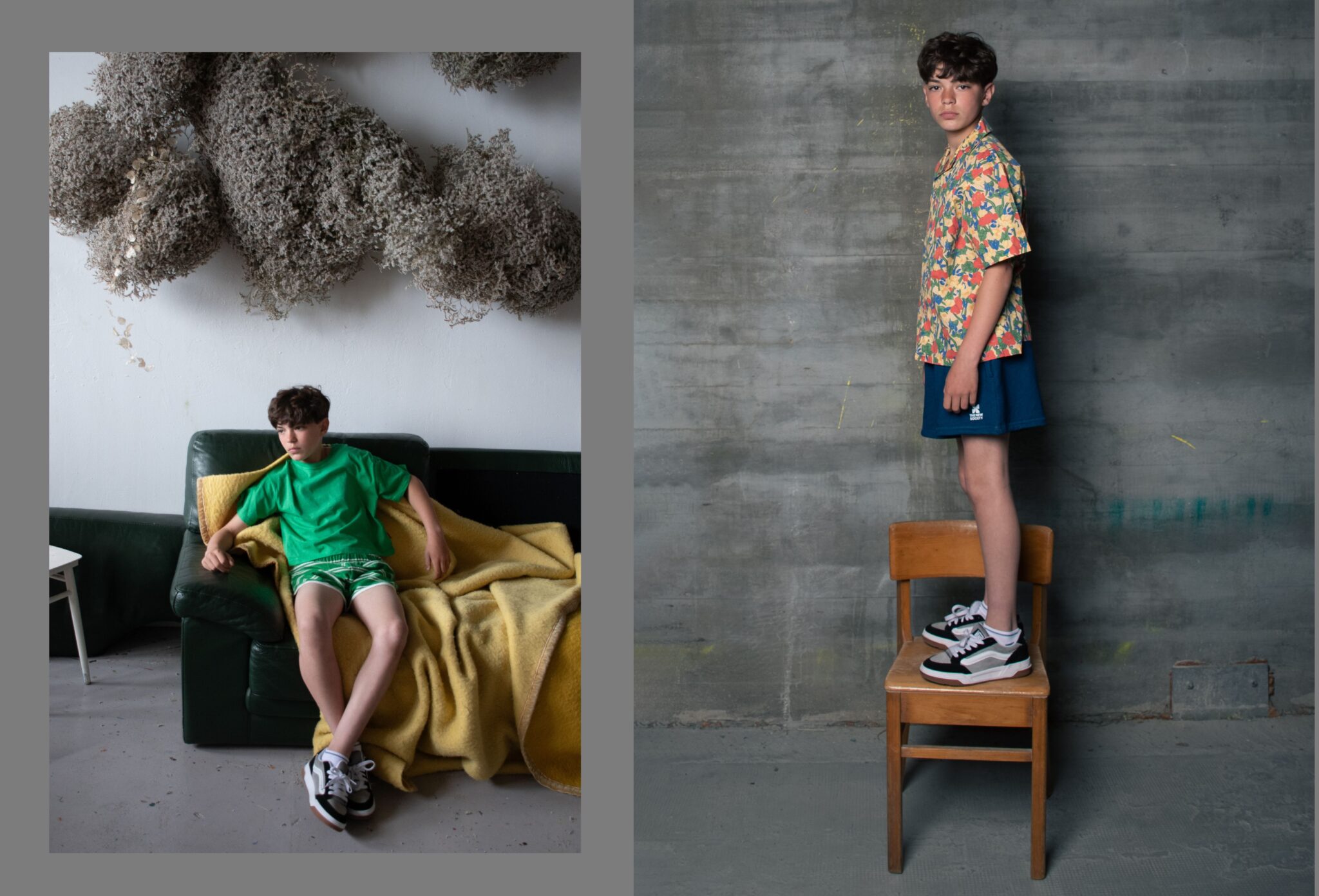 Boy in green and blue summer looks, sitting on a dark green sofa with a yellow blanket and standing on a wooden chair against a textured grey wall, in the Friends Forever kids fashion editorial photographed by Danique Daemen, Scimparello Magazine.