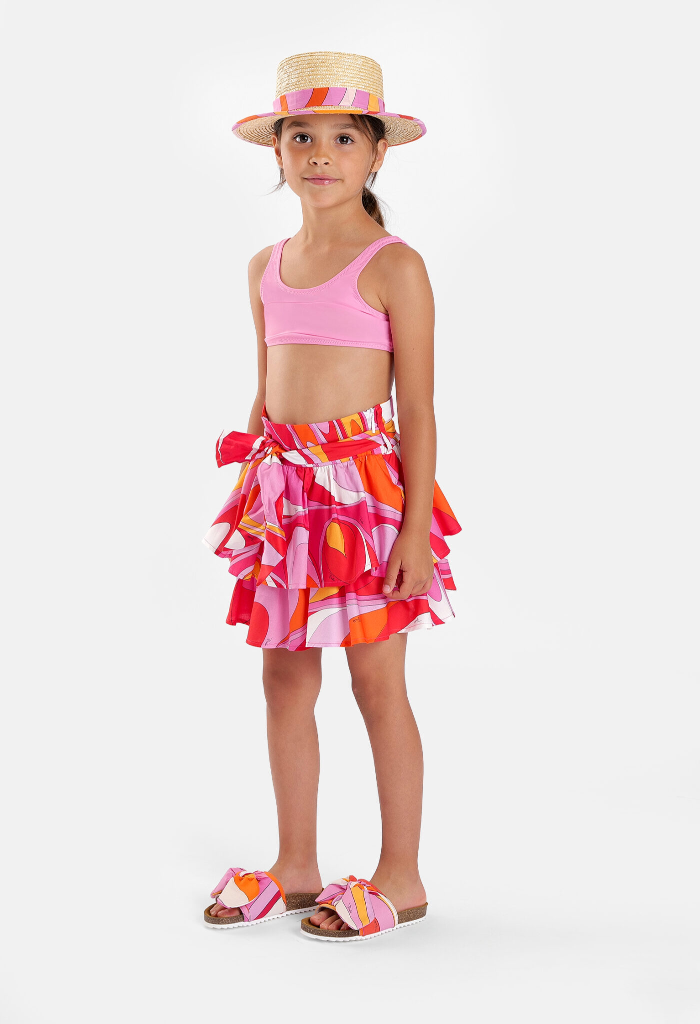 Girl wearing a Pucci Junior SS26 tiered summer skirt in the iconic Marmo print, paired with a pink crop top, straw hat and colourful sandals.