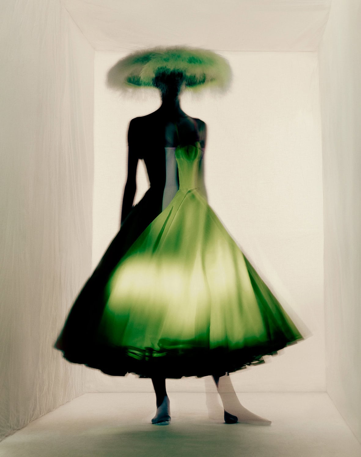 A blurred silhouette of a model wearing a luminous green couture gown inside a white room, photographed by Paolo Roversi with a dreamlike long-exposure effect.