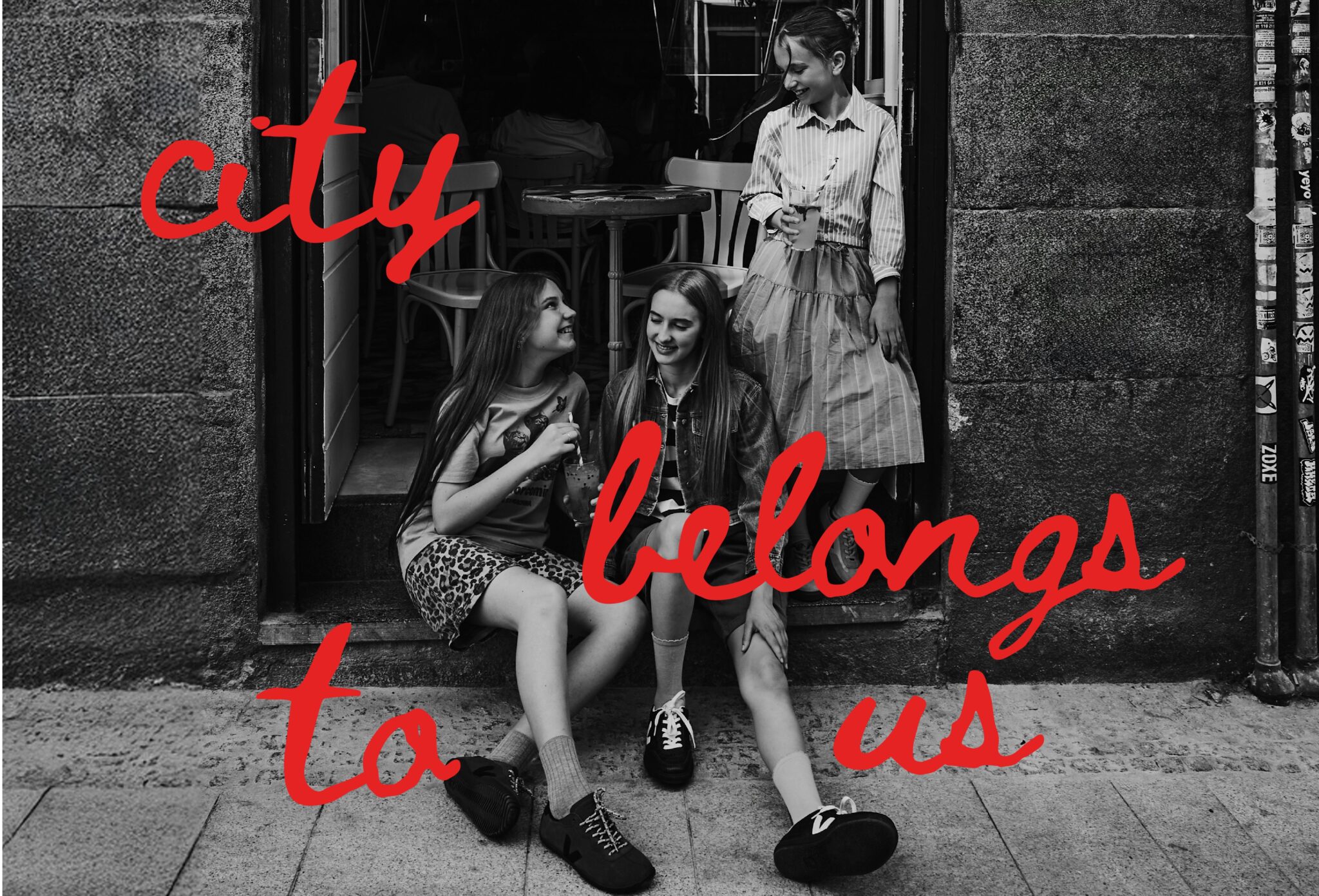 Black and white teen fashion editorial City Belongs to Us photographed by Sandra Martinez and Mara Rodriguez, featuring three girls sitting outside a café in an urban street scene for Scimparello Magazine.