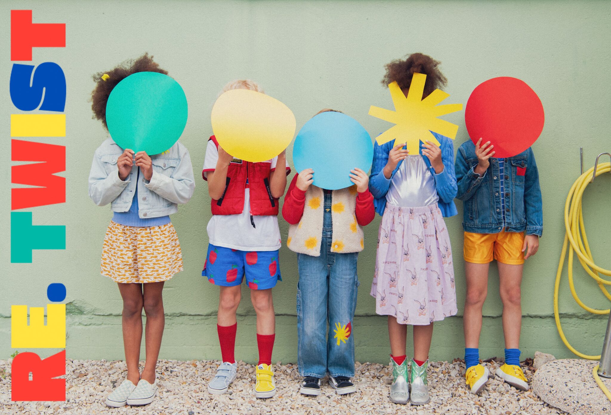 Kids fashion editorial RE.Twist photographed by Emmanuelle Lhote, featuring children wearing colourful upcycled clothes and holding graphic shapes in front of a green wall for Scimparello Magazine.