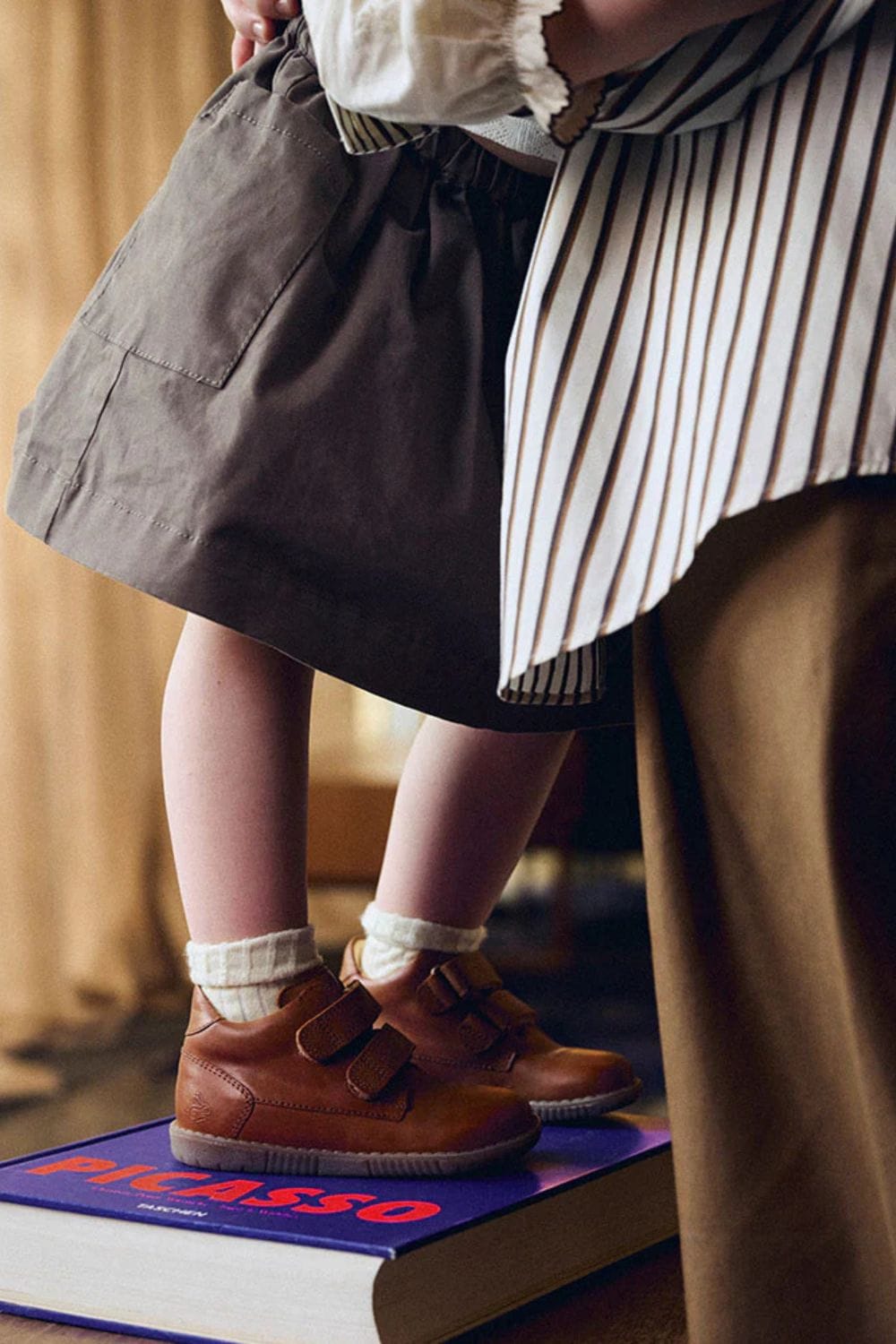 Close-up of a child wearing classic brown Bundgaard leather shoes while standing on a stack of books, showcasing the timeless craftsmanship and design featured in the Bundgaard Generations campaign.