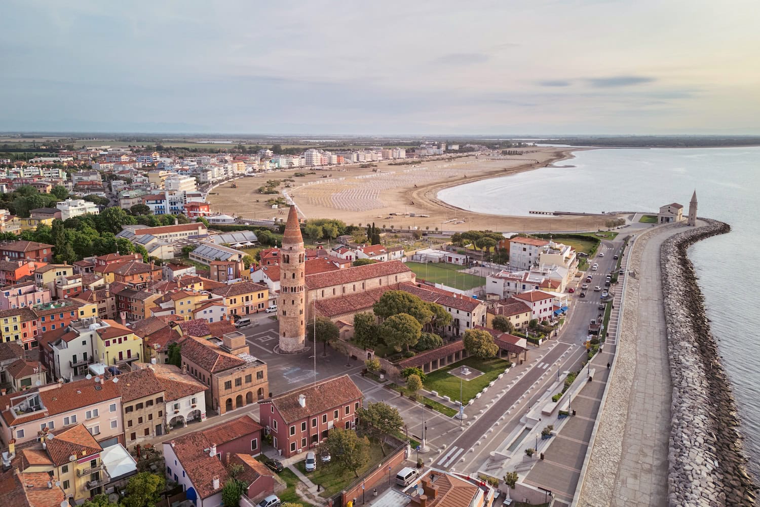 Aerial view of the historic centre of Caorle, Italy, with its colourful houses, bell tower, sandy beach and Adriatic coastline, perfect for a family holiday.