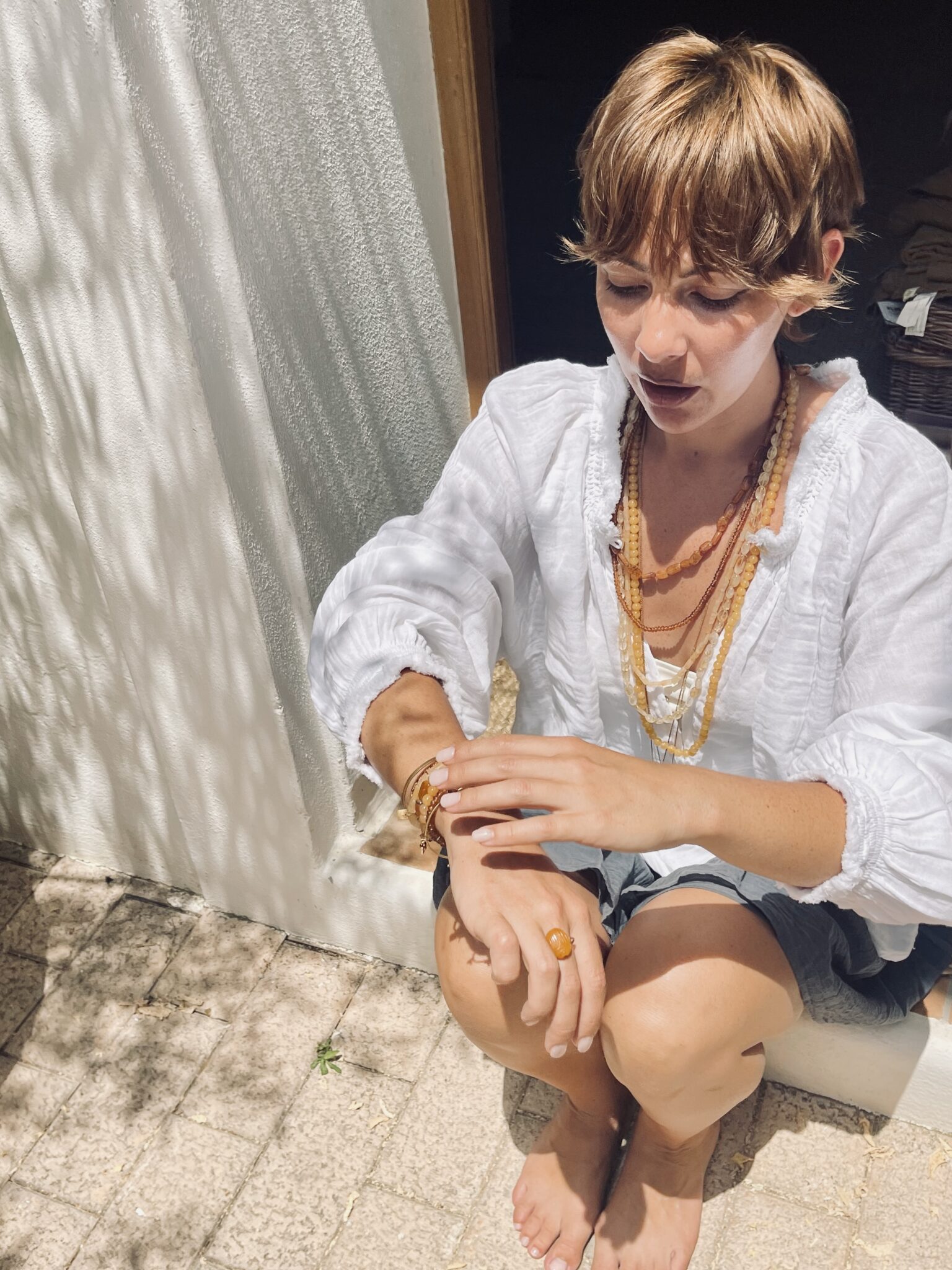 N°74 jewelry handmade in India, featuring layered amber-toned natural stone necklaces, bracelets and a statement ring worn with a white cotton blouse for Scimparello Magazine.