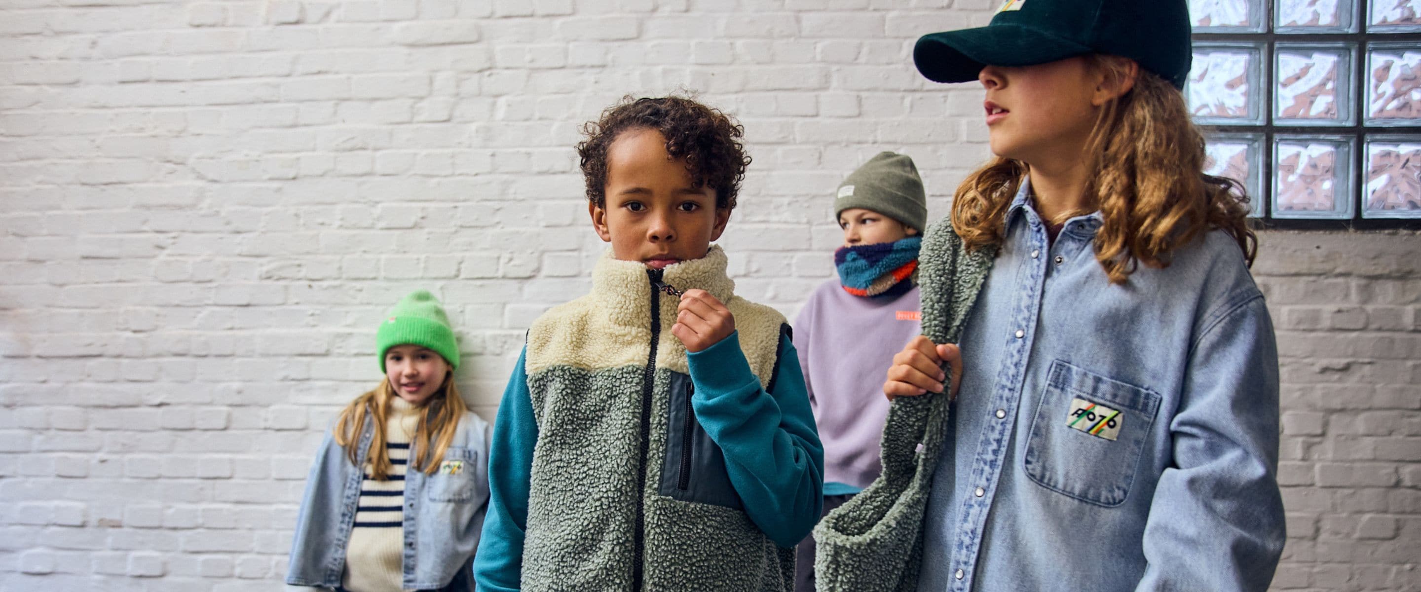 Group of children laughing together in colorful fleece vests, oversized sweatshirts and denim outfits for autumn.