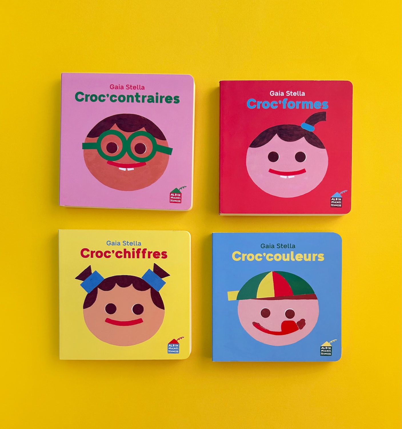 Four colourful board books from Gaia Stella's Yum Yum Series displayed on a bright yellow background. The collection includes Croc'Contraires, Croc'Formes, Croc'Chiffres and Croc'Couleurs, featuring minimalist illustrated faces and introducing toddlers to opposites, shapes, numbers and colours through playful design.