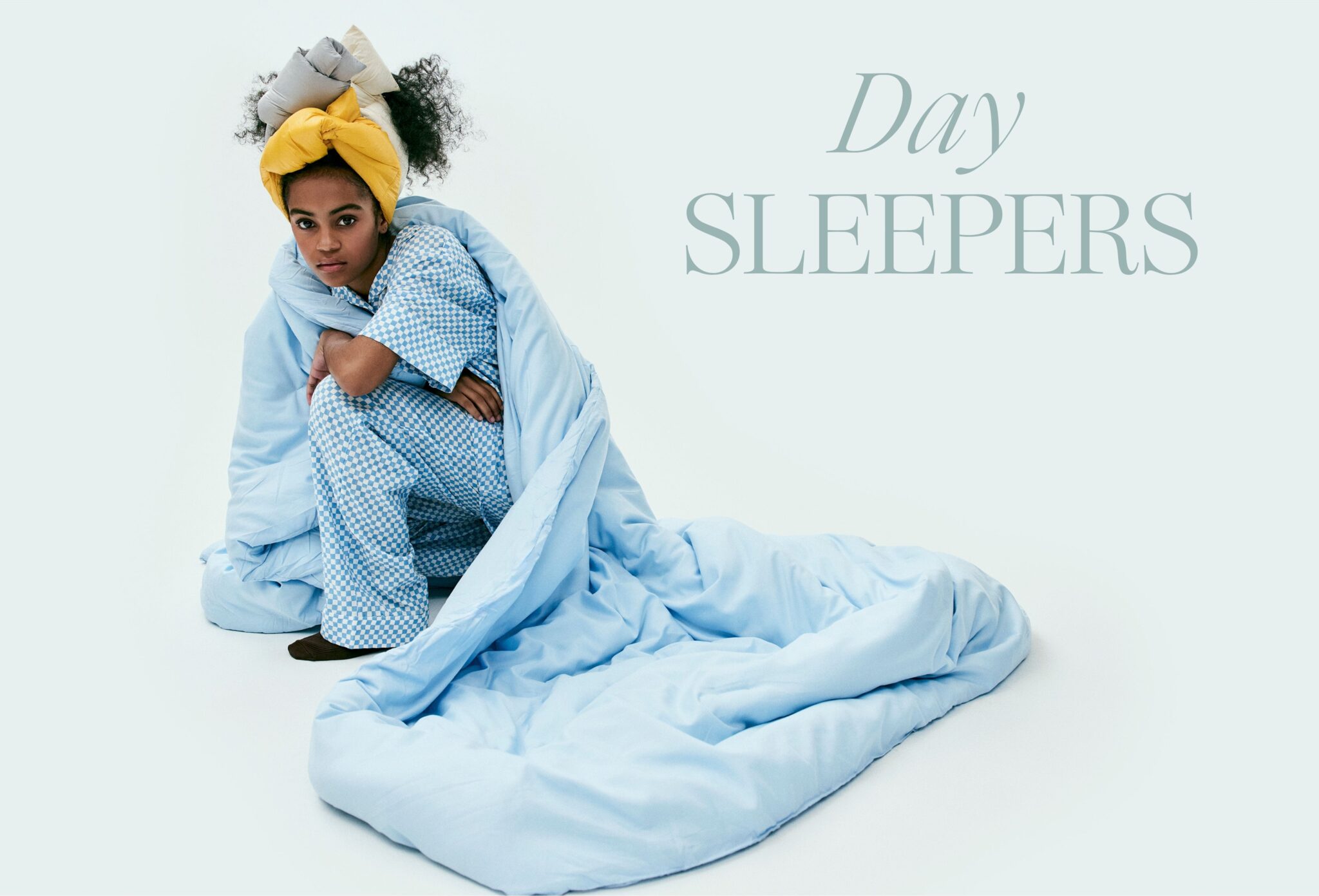 Kids fashion editorial Day Sleepers photographed by Erin Foster and styled by Julie Williams, featuring a girl wrapped in pale blue bedding and wearing blue check pyjamas for Scimparello Magazine.