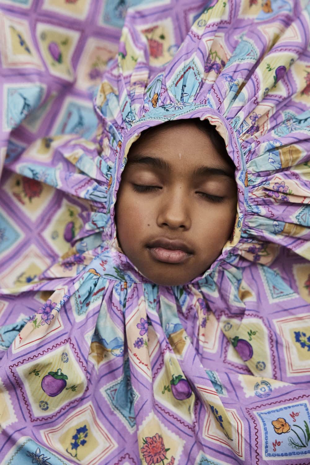 Child resting with eyes closed, surrounded by a colorful floral-print Maison Mangostan garment.