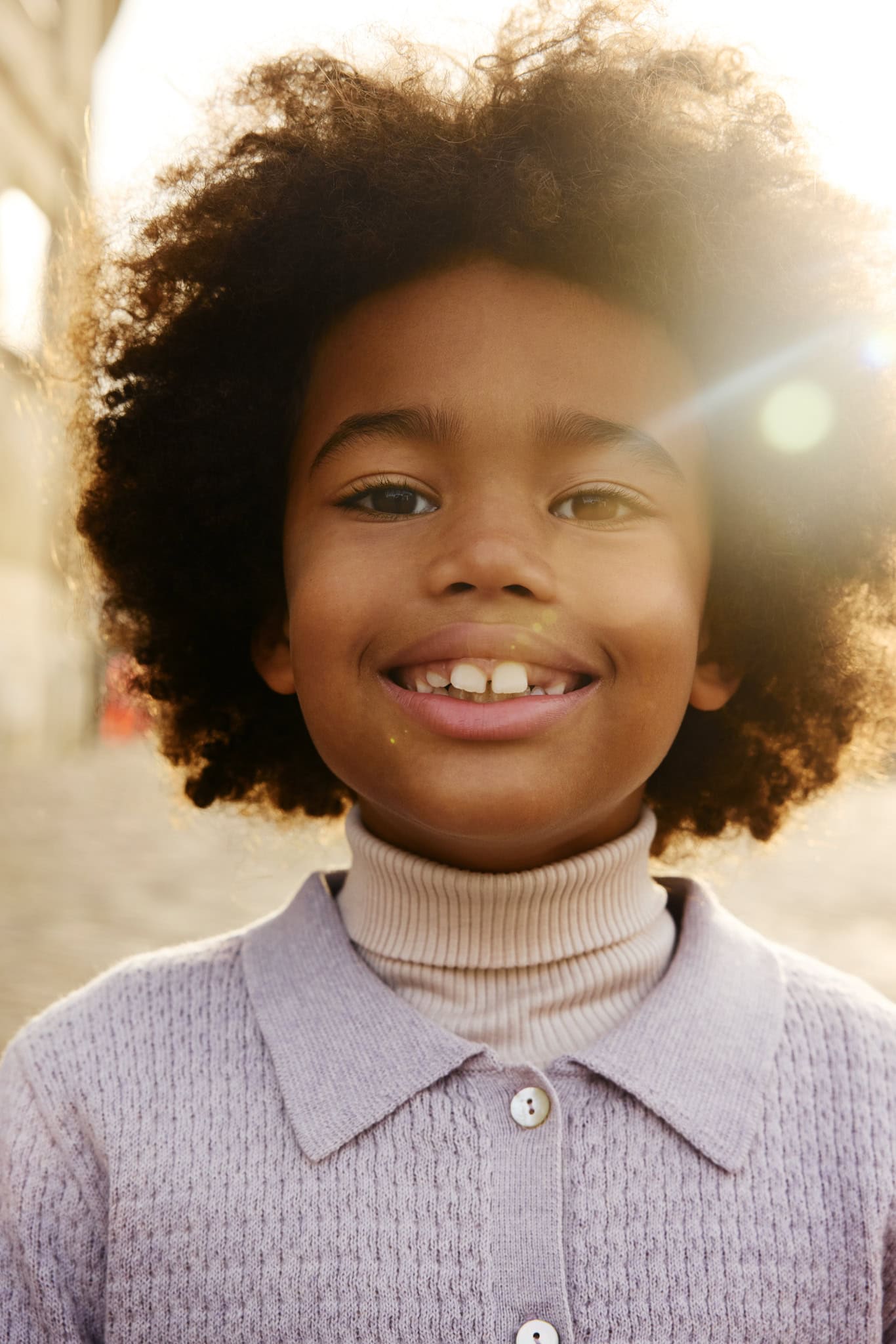 Child wearing a soft lilac knitted cardigan and ribbed turtleneck from the Minimalisma FW26 collection, smiling in warm winter sunlight.
