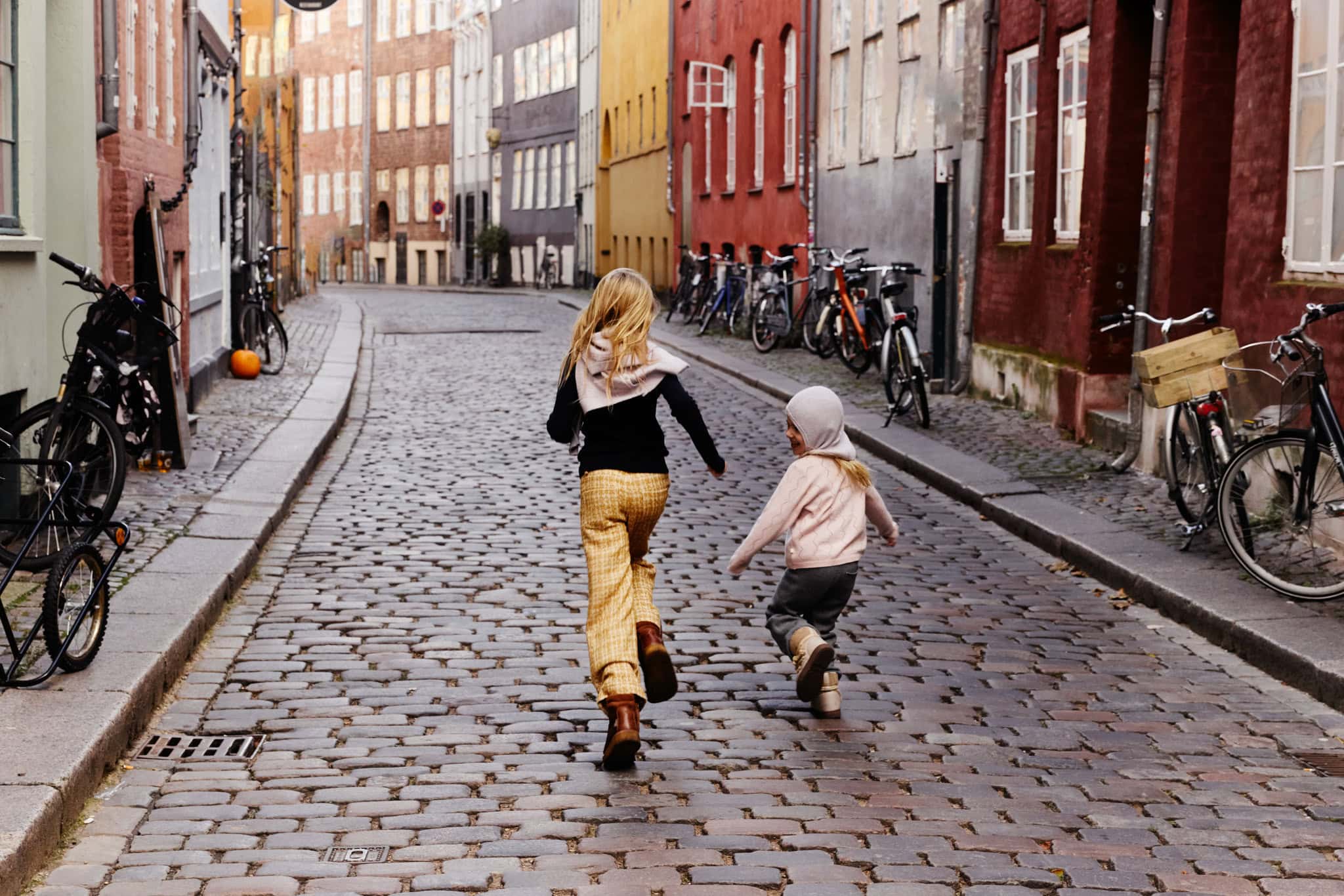 Two children running through a cobblestone street in Copenhagen wearing Minimalisma FW26 knitwear and trousers.