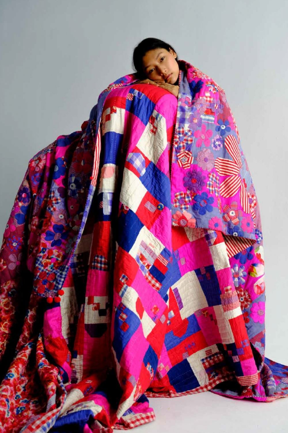 A child wrapped in a vibrant patchwork quilt featuring bold pink, red, blue and floral patterns from péro Home.