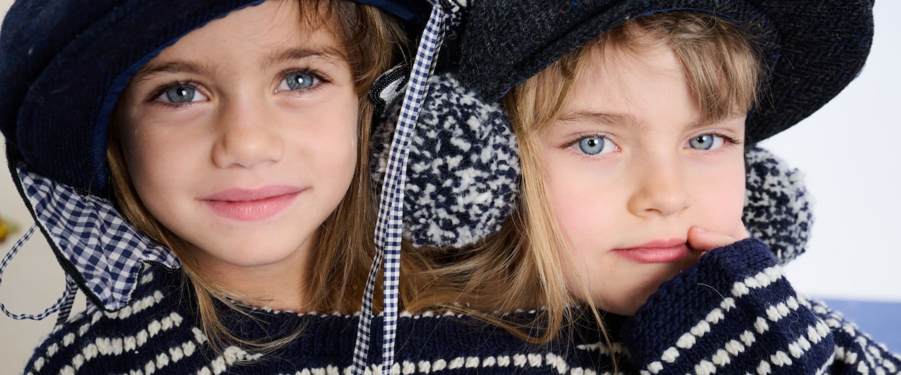 Close-up portrait of two girls wearing navy and white striped knitwear and matching dark hats.