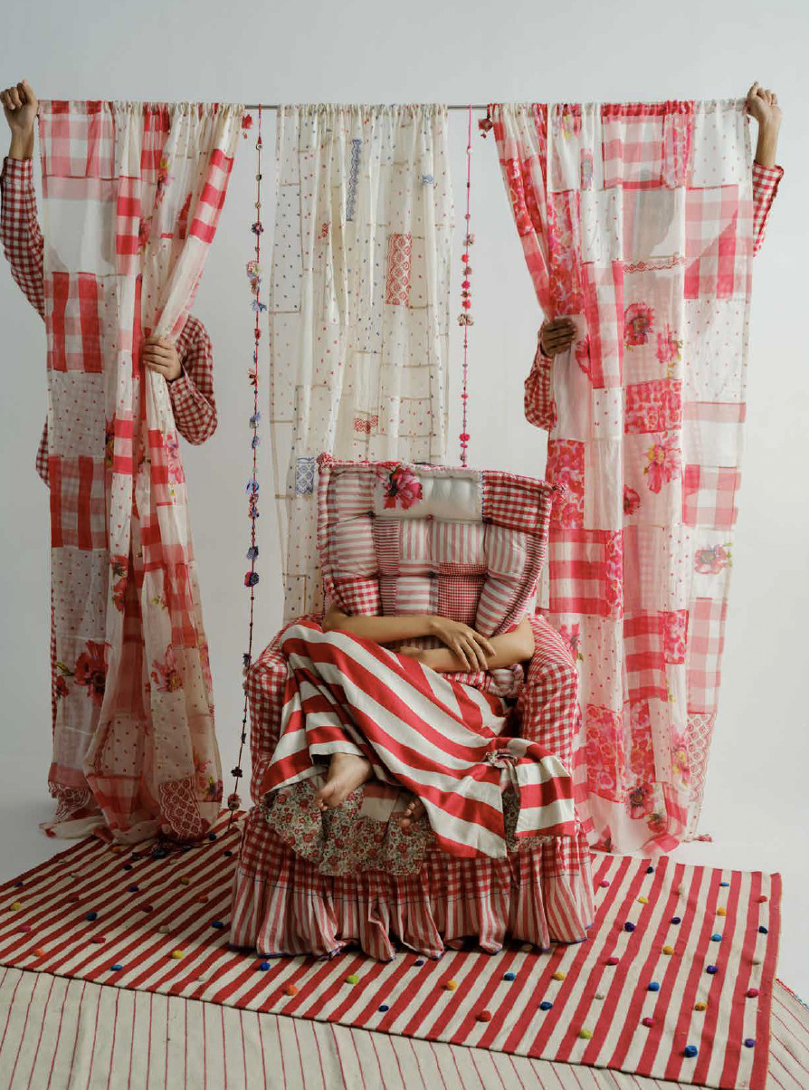 Person sitting in a patchwork armchair surrounded by red and white checked textiles, striped rugs and floral fabrics from péro Home.