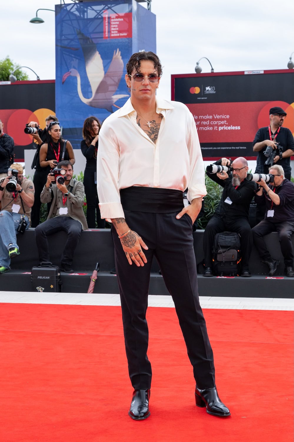 Italian singer Achille Lauro posing on the red carpet at the Venice Film Festival in a white shirt, black trousers and black boots.