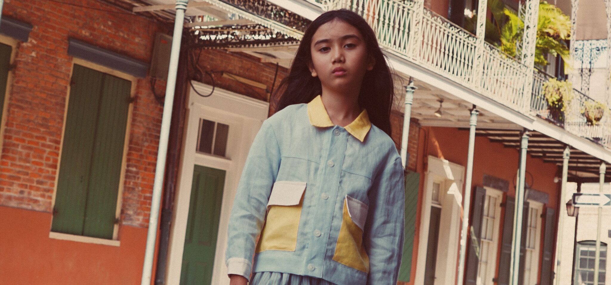 An Afternoon in New Orleans fashion editorial by Dope Style Kid x Jennifer Grasso, featuring a girl in layered green, blue and yellow looks photographed against the colourful architecture of New Orleans for Scimparello Magazine.