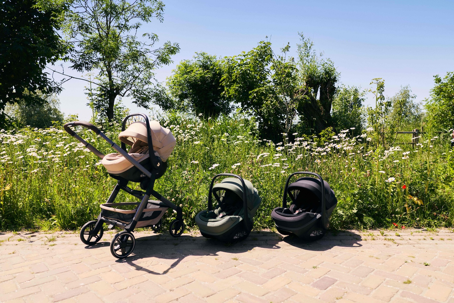 Joolz stroller with Pebble Slide Pro car seat in a sunny outdoor setting, alongside two additional car seats in Forest Green and Space Black.