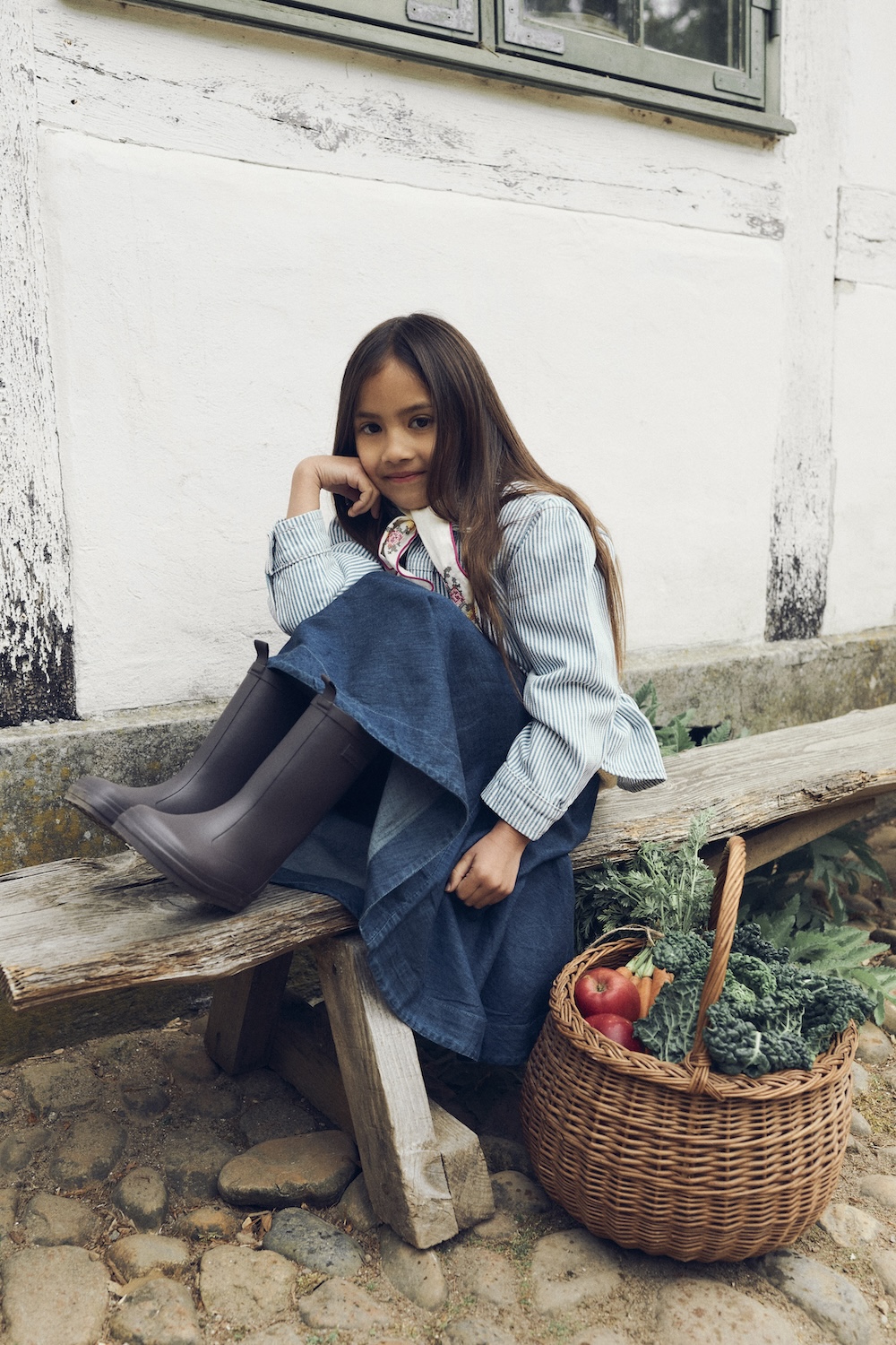 Girl wearing denim and black Bundgaard rain boots beside a basket of vegetables.