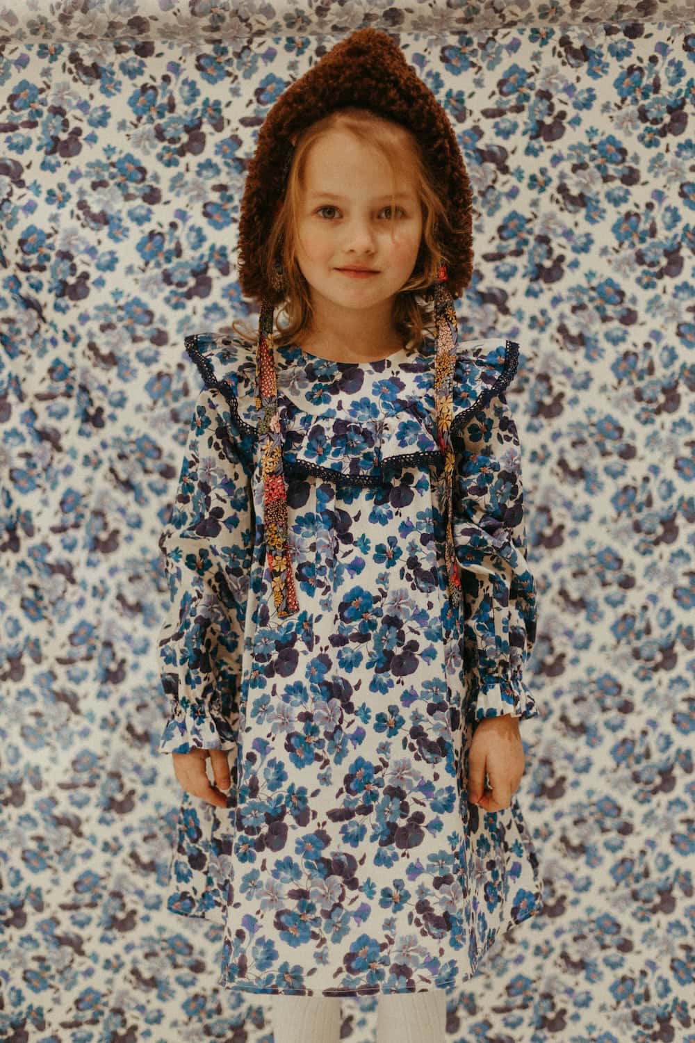 Paade Mode THE STARBOUND FW26 collection, featuring a girl in a blue floral dress and textured knit hood against a matching floral backdrop for Scimparello Magazine.
