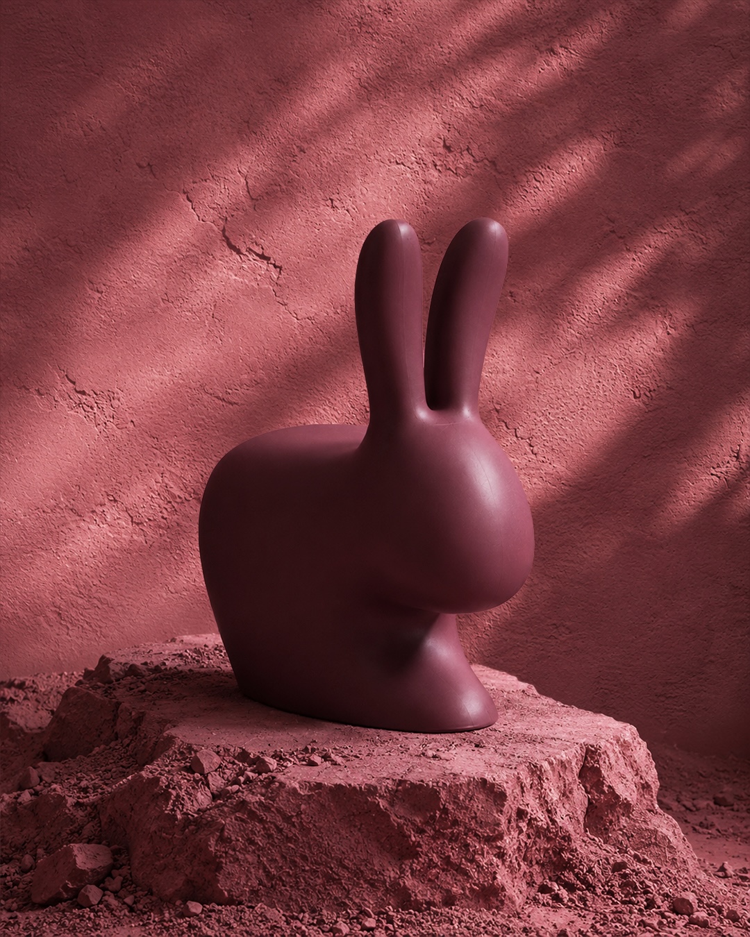 Qeeboo’s Rabbit Chair in Indian Red, featuring its iconic rabbit-ear silhouette, photographed against a textured terracotta-red backdrop.