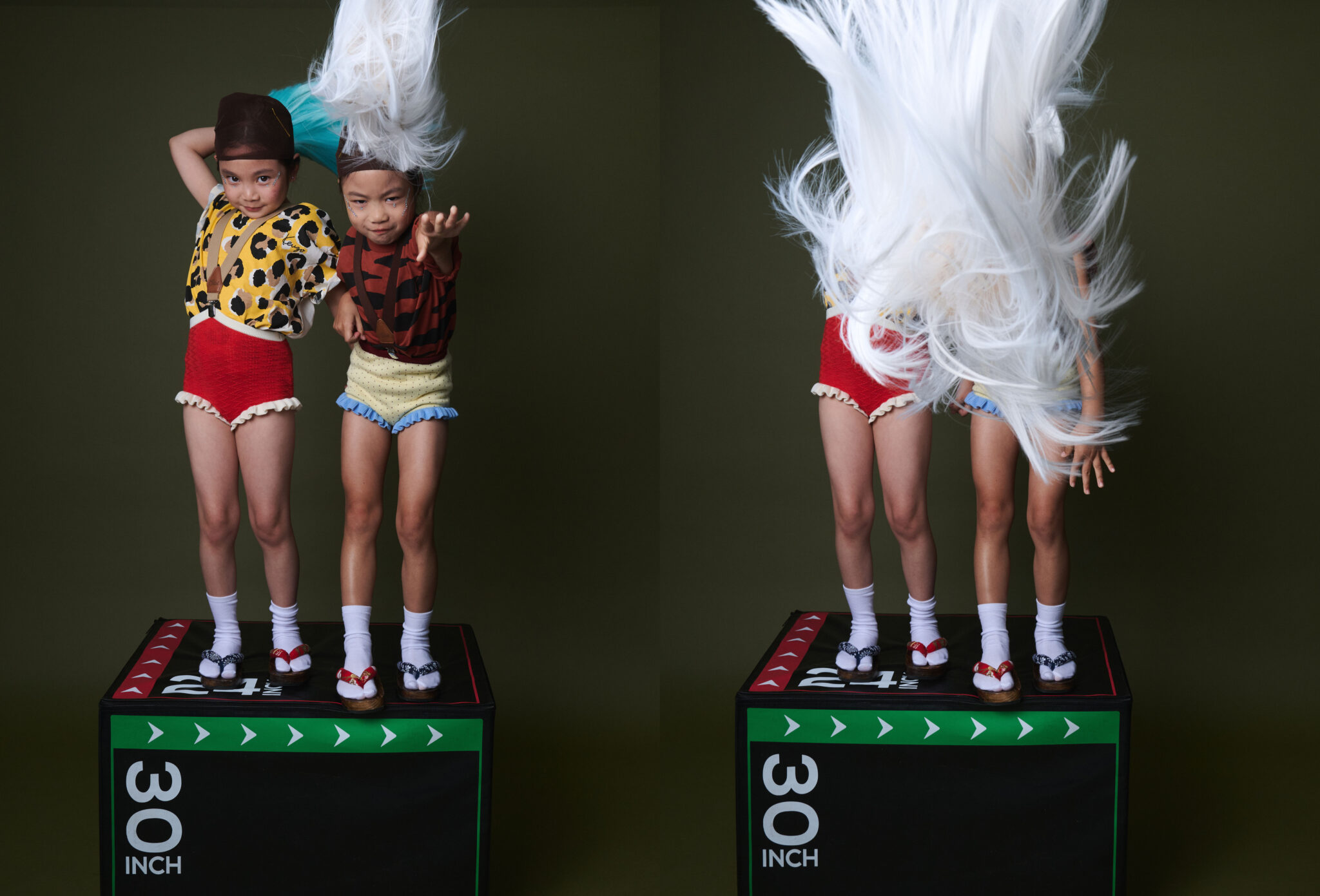 Two girls on a plyo box tossing their wigs into the air, the white wig flying above their heads