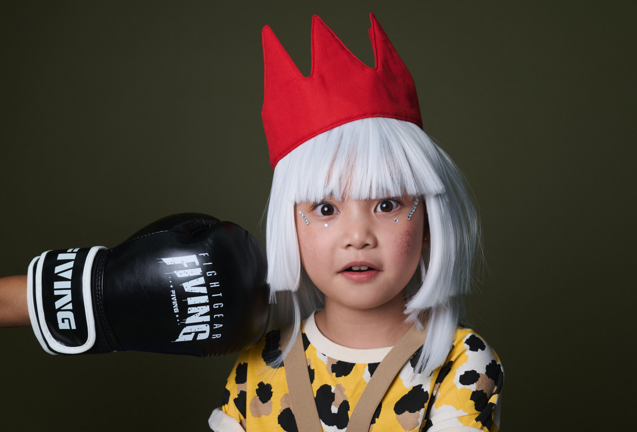 A girl in a white wig and red fabric crown looking surprised as a boxing glove comes in from the side