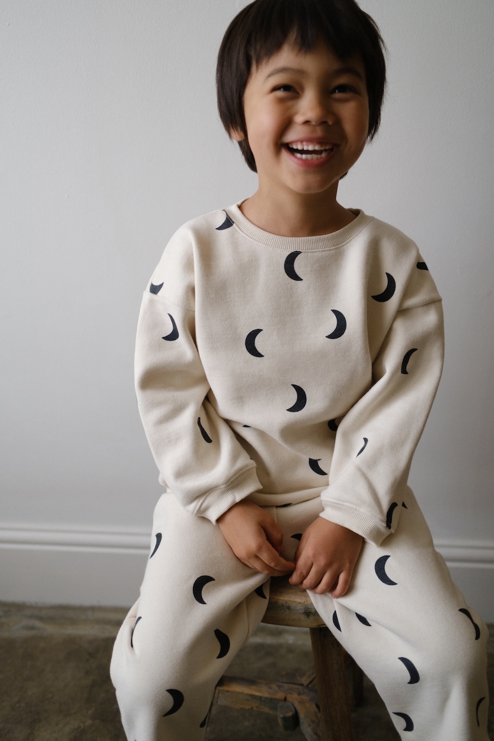 Child wearing an Organic Zoo x BINIBAMBA cream sweatshirt and trousers covered in a black crescent moon print.