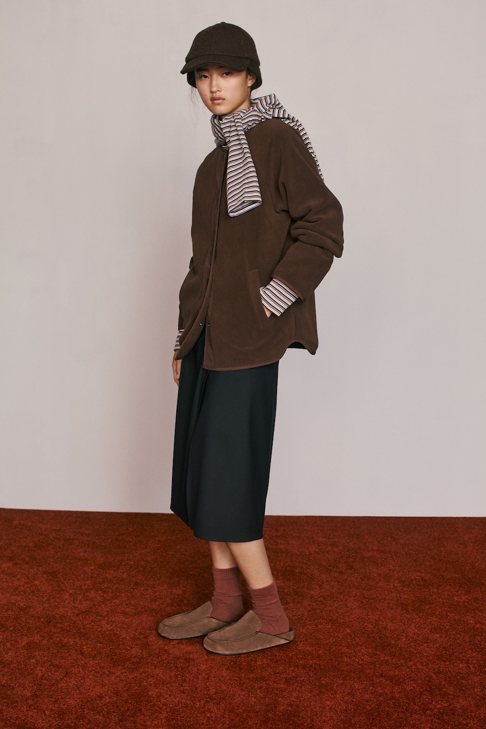 Woman wearing a brown jacket, striped scarf and bucket hat with a dark skirt, dusty pink socks and brown loafers from Caramel for Zara.