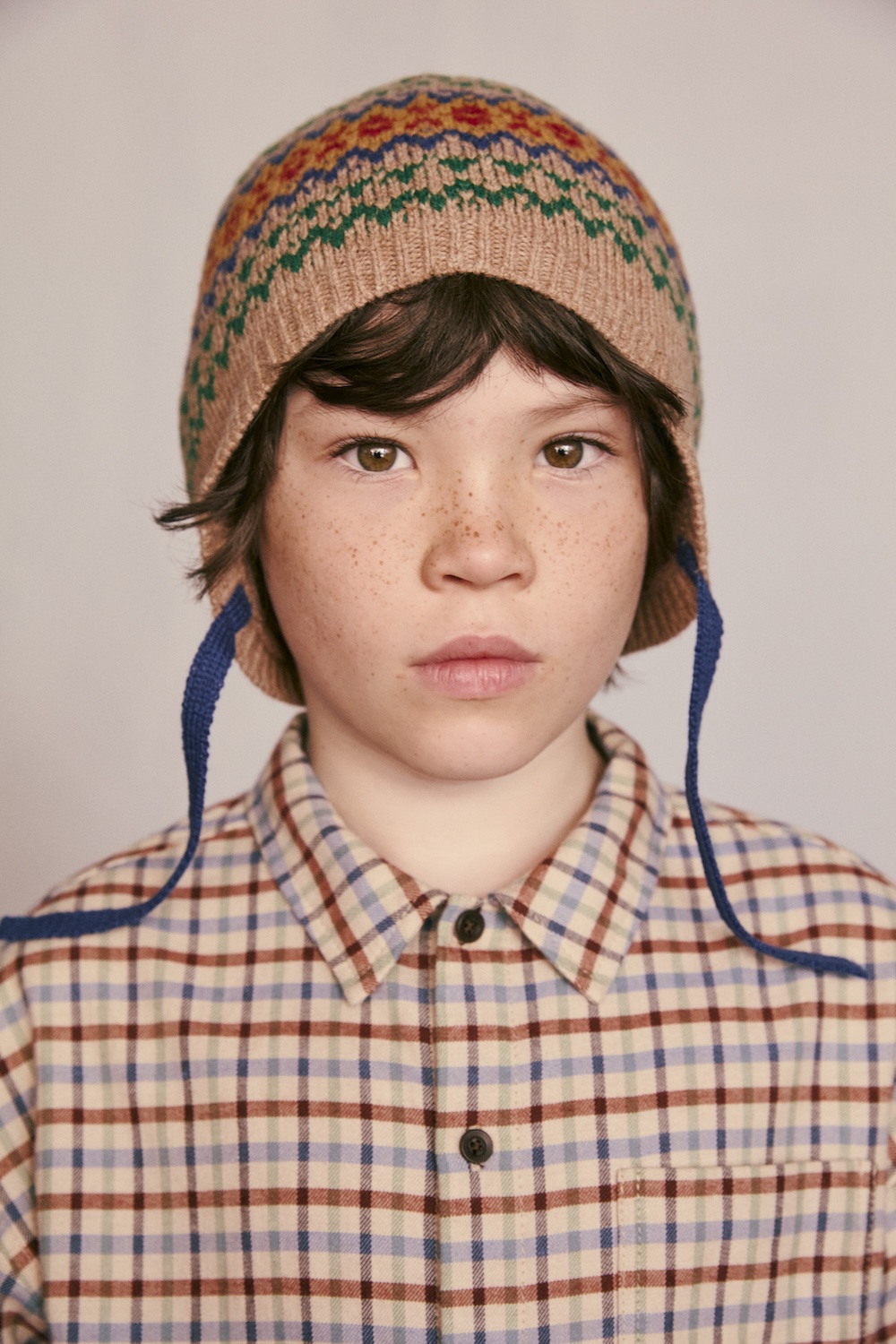 Close-up portrait of a child wearing a colourful Fair Isle knit hat and a checked shirt from Caramel for Zara.